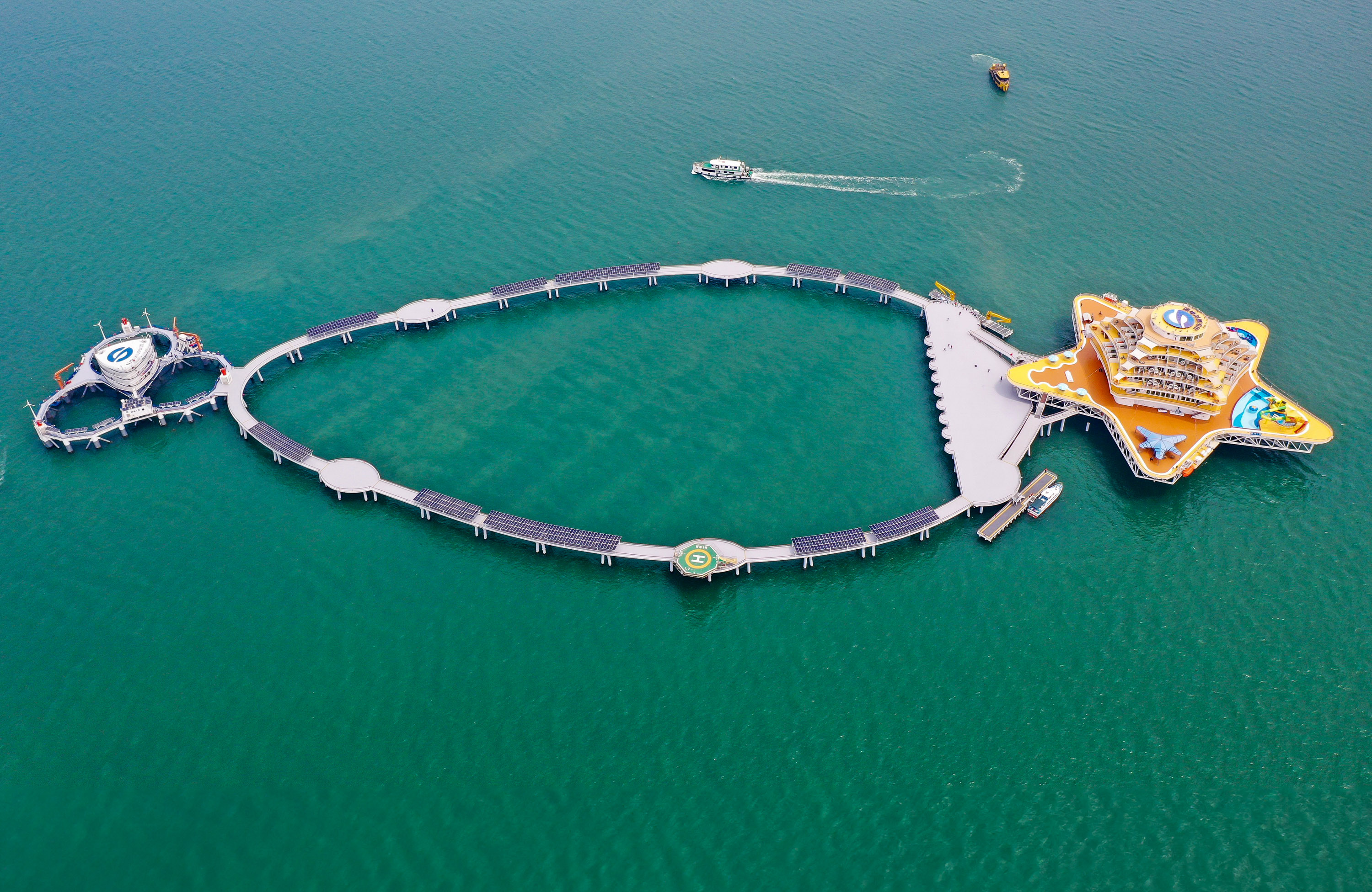 A complex shaped like a star with an oval of solar panels connecting it to a second hub made of three linked circles in the ocean