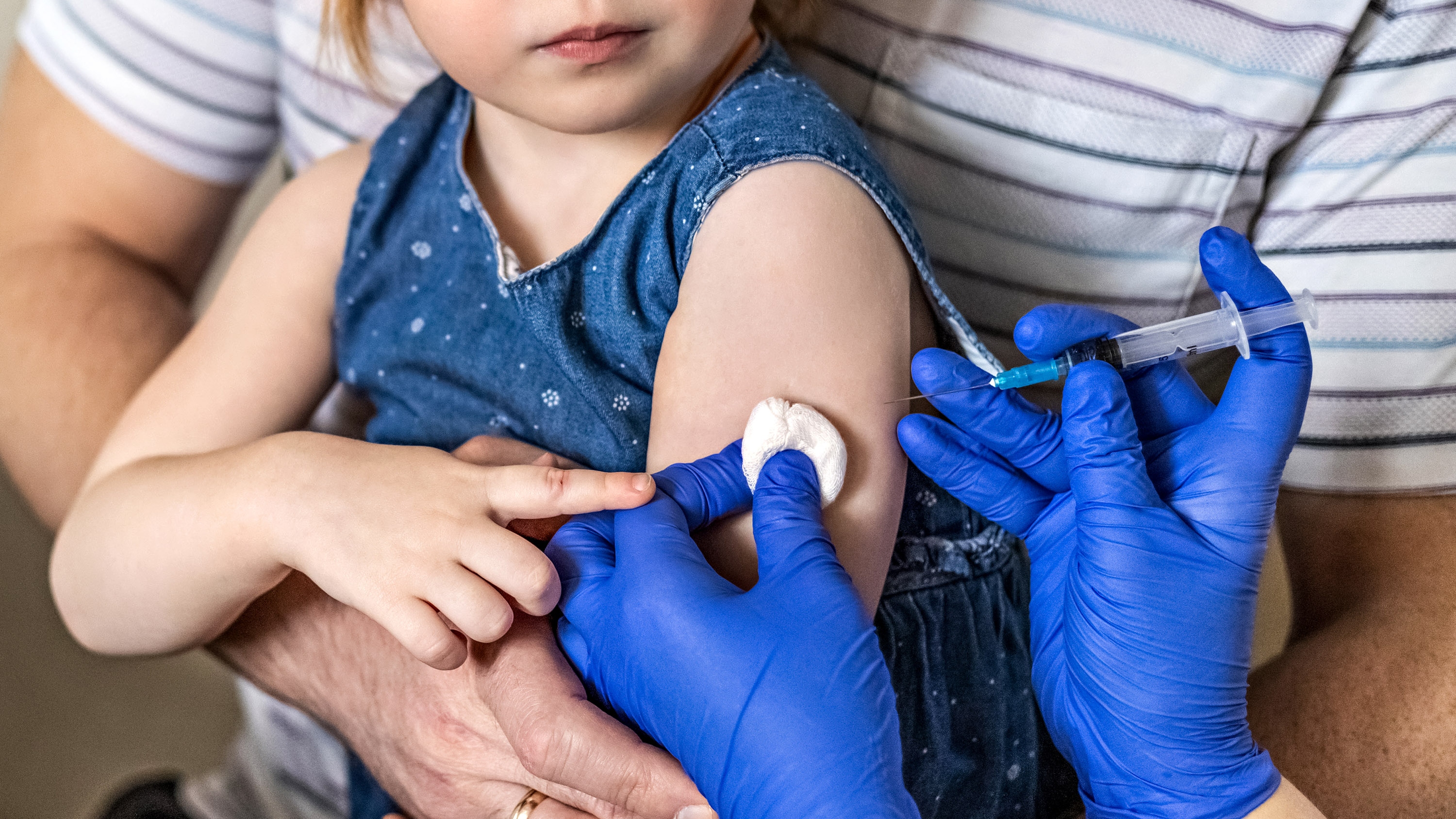closeup on a little girl held by her father as a vaccine is about to jab her arm