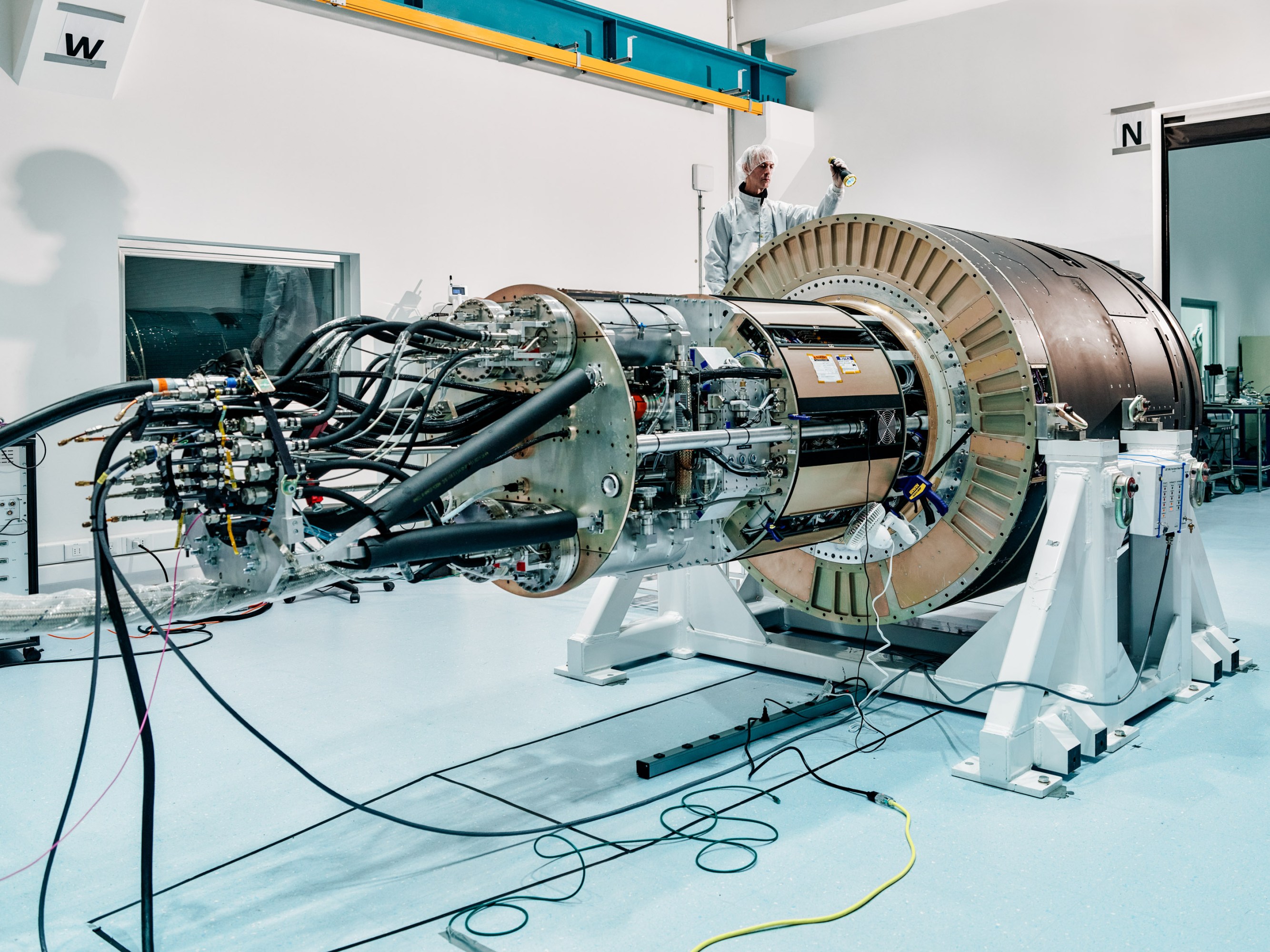 a man in a clean room suit shines a light at a device that spans the room.